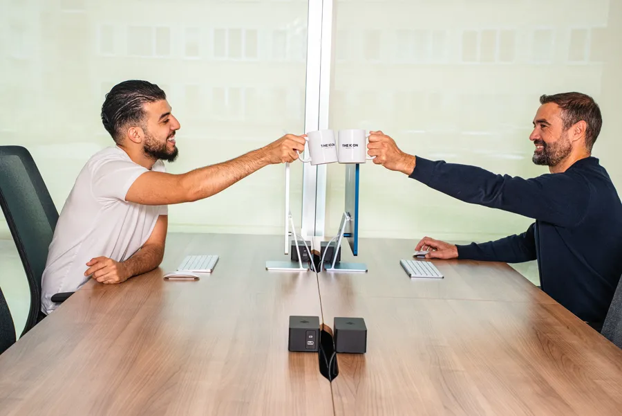 Deux collègues trinquant avec des mugs THE ICON de part et d'autre d'un bureau